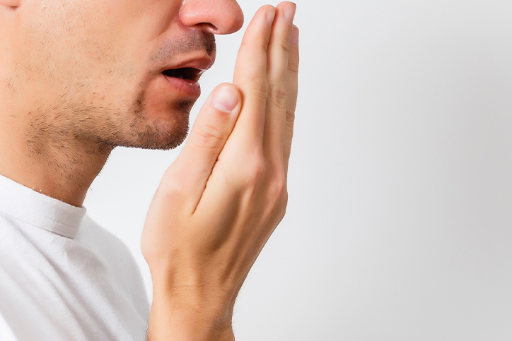 A man cupping his hand over his mouth, checking his breath