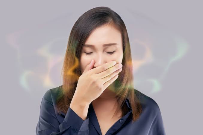 A woman covering her mouth, with a faint odour cloud around her face